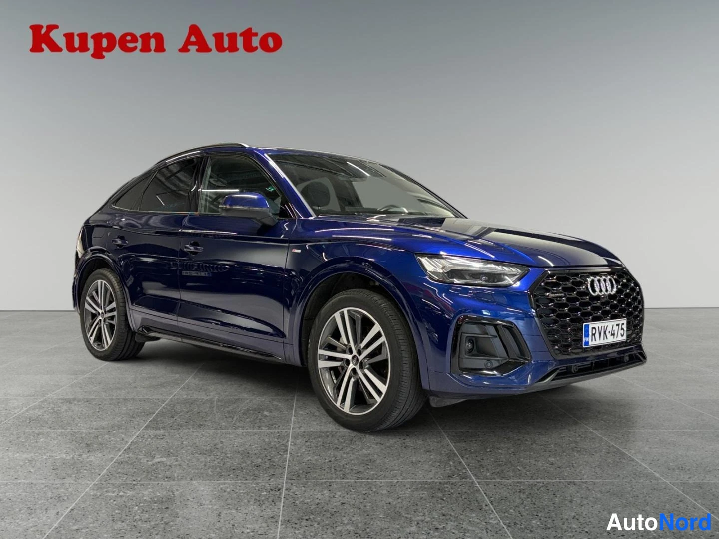 Etuviisto, nokka oikealle: Sininen Audi Q5 Sportback kulmittain edestä oikealta kuvattuna myyntihallissa.