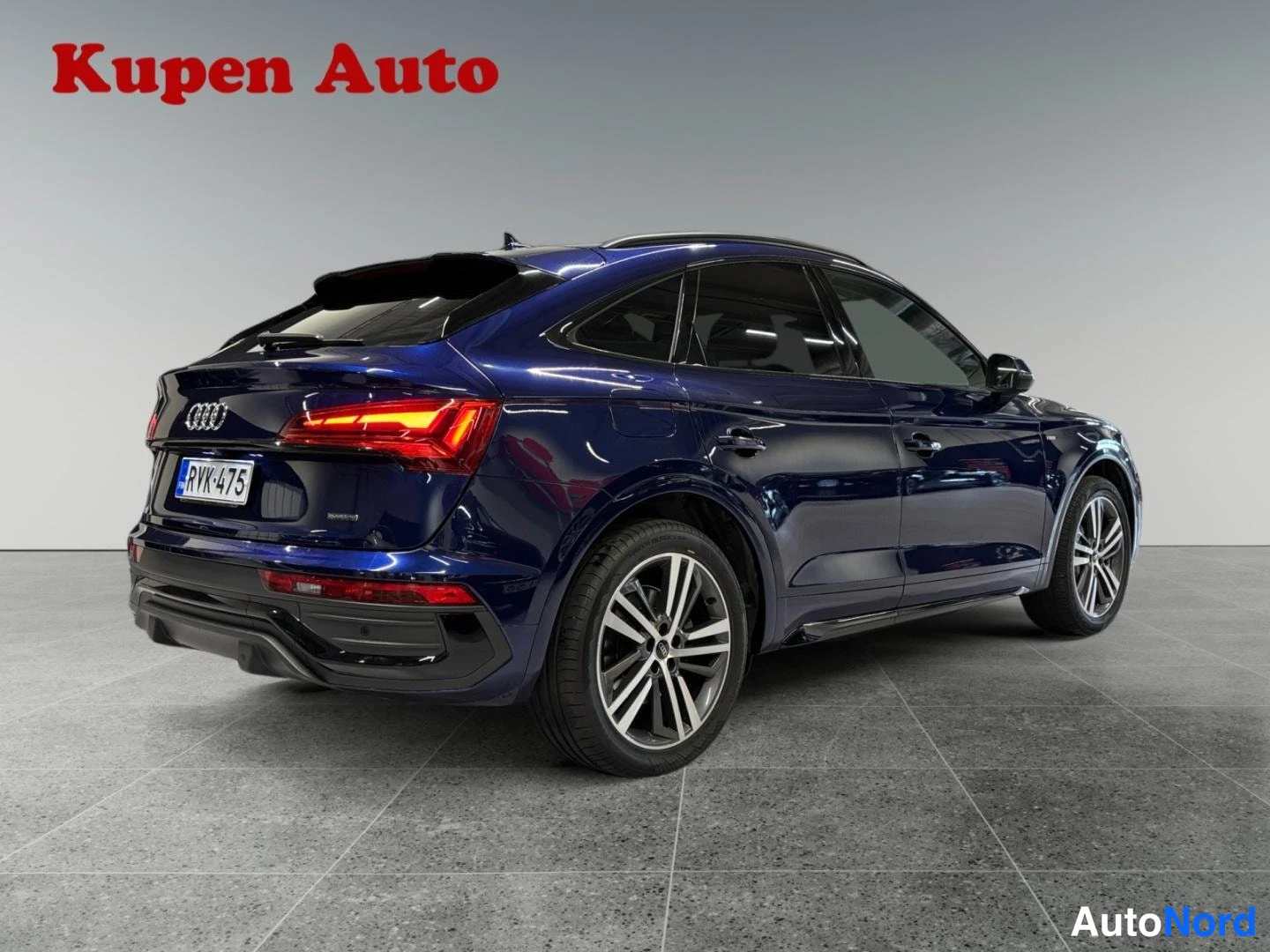 Takaviisto: Sininen Audi Q5 Sportback kulmittain takaa oikealta kuvattuna myyntihallissa.