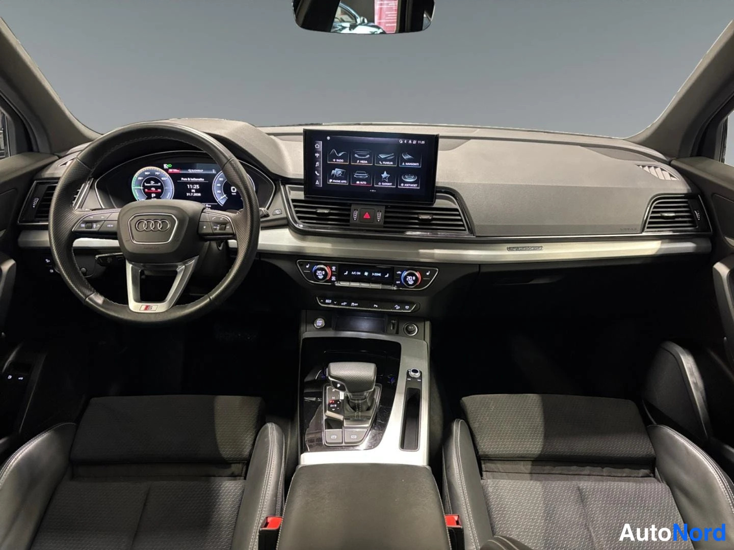 Yksityiskohta: Auton sisätilat etupäädystä: Audi-ohjauspyörä vasemmalla, digitaalinen mittaristo, keskellä kosketusnäyttö ja kaksipaikkainen etupenkki, musta verhoilu.