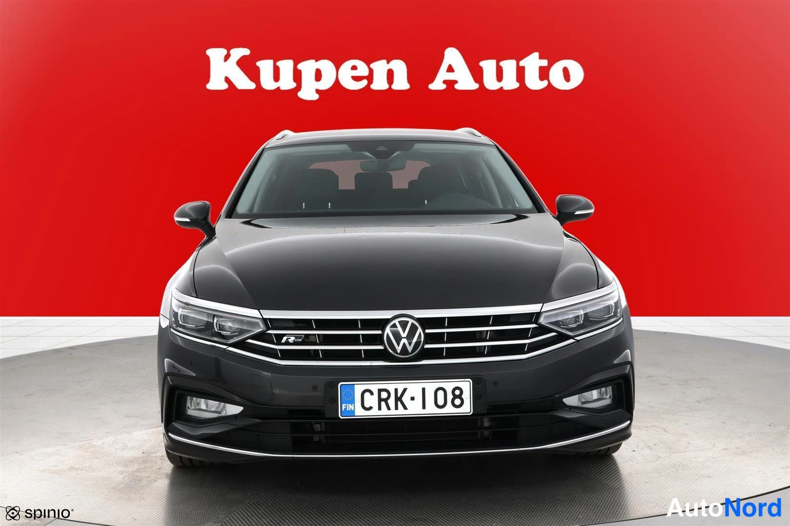 Edestä: Tummansininen Volkswagen Passat -farmari suoraan edestä, rekisteritunnus, taustana punainen Kupen Auto -tausta.