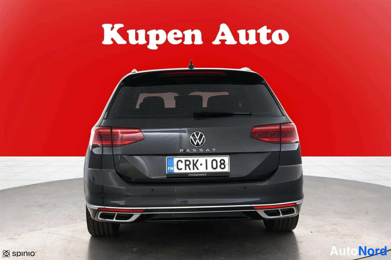 Takaa: Auton takaosa suoraan takaa: Volkswagen-merkki, PASSAT-teksti, rekisterikilpi, punaiset takavalot ja kromikoristeet puskurissa punaisella taustalla.