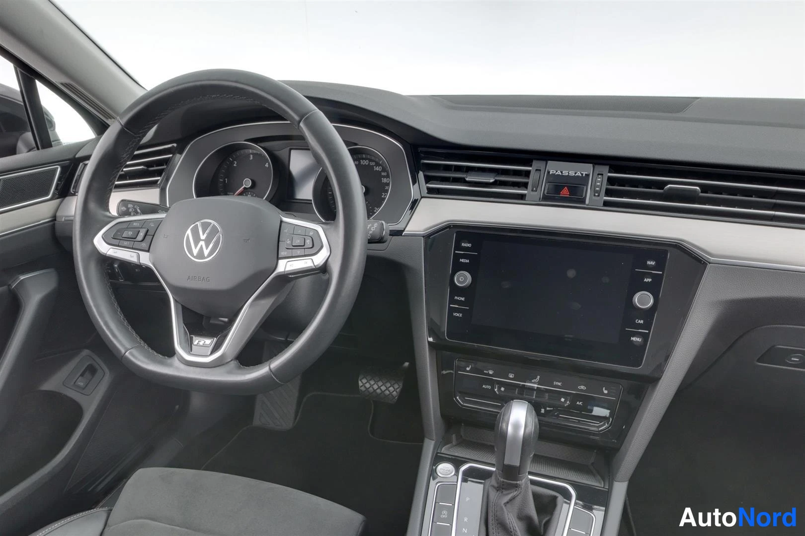 Muu: Lähikuva ohjaamosta: Volkswagen-ohjauspyörä ilmatyynymerkinnällä, mittaristo, PASSAT-merkitty ilmastointipaneeli, radio/kosketusnäyttö ja vaihteenvalitsin.