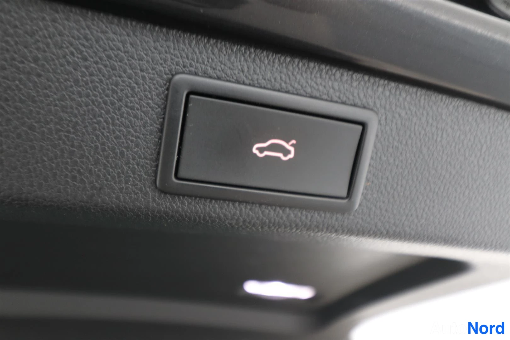 Yksityiskohta: Sisätilakuvan detalji: tumma katto/upholsteria ja pieni painike, jonka symbolina on auto. Ei näkyvää auton korin osaa.