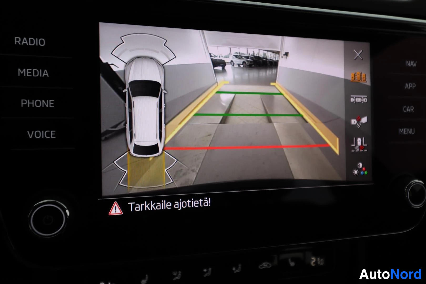 Muu: Infotainment-näyttö, joka näyttää peruutuskameran kuvan ja teksti 'Tarkkaile ajotietä!'.