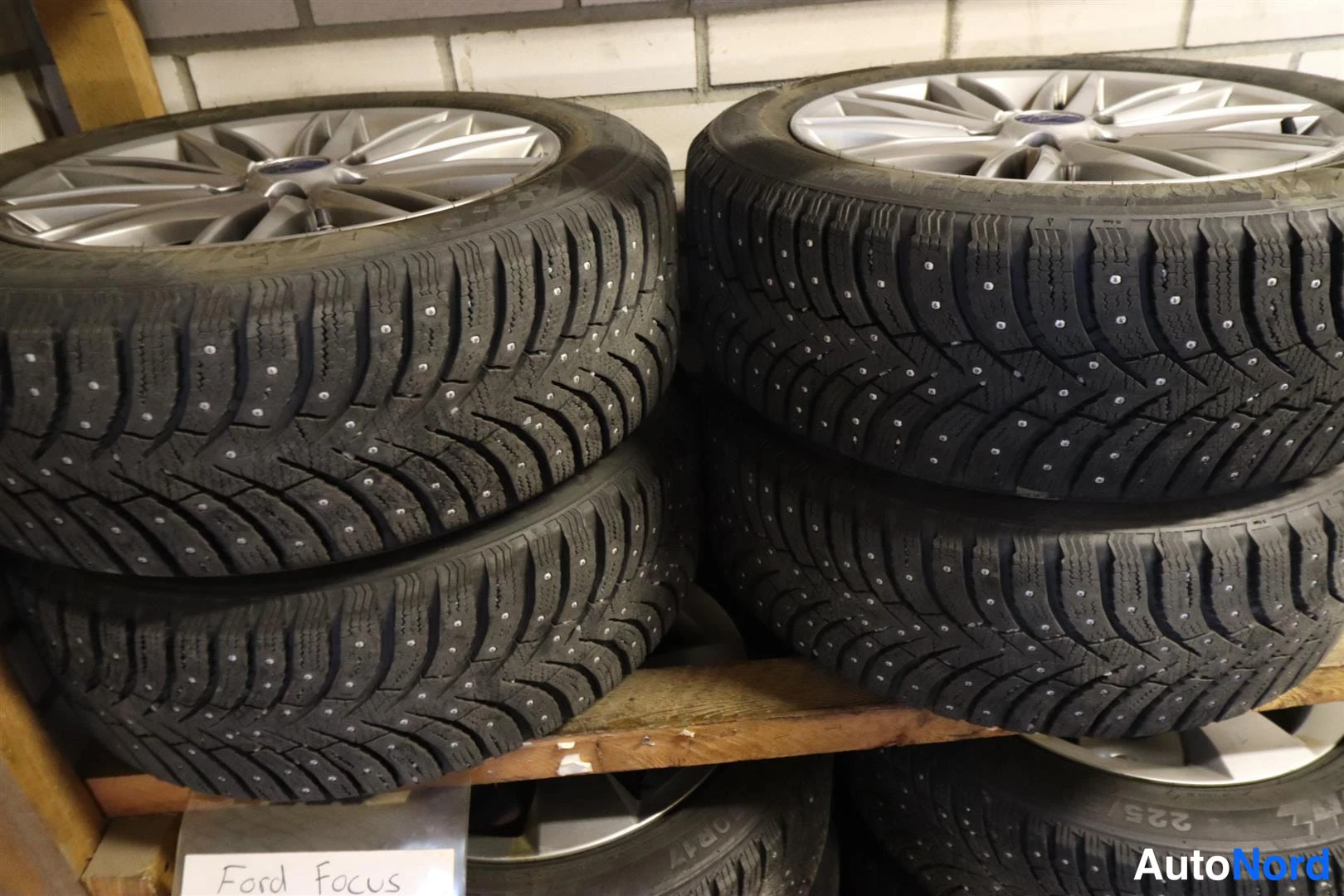 Yksityiskohta: Neljä nastarenkaita vanteilla hyllyllä, alapuolella lapulle kirjoitettu 'Ford Focus'.