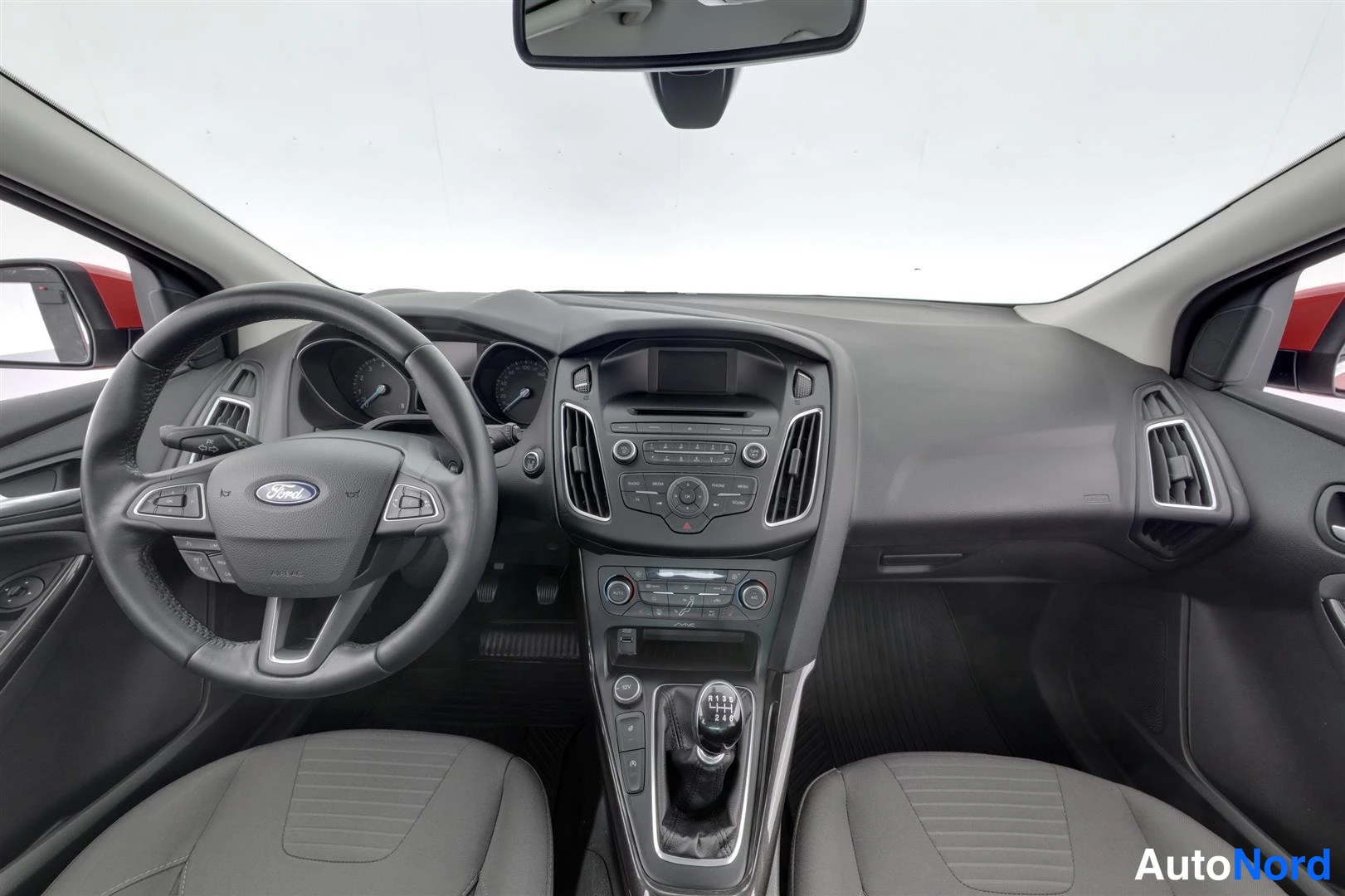 Muu: Ford Focusin tumma ohjaamo edestäpäin: ratkossa Ford-logo, keskikonsolissa kosketusnäyttö ja manuaalivaihteen keppi.