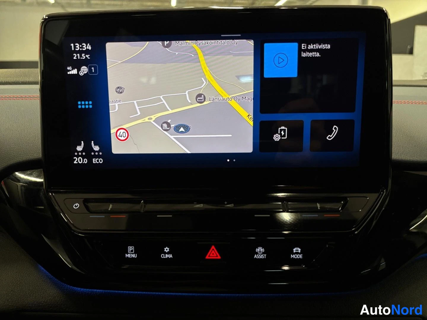 Muu: Auton keskikonsolin infotainment-näyttö, jossa näkyy navigointikartta, aika 13:34, lämpötila 21,5 °C ja ECO-tila, alapuolella fyysiset painikkeet MENU, CLIMA, A
