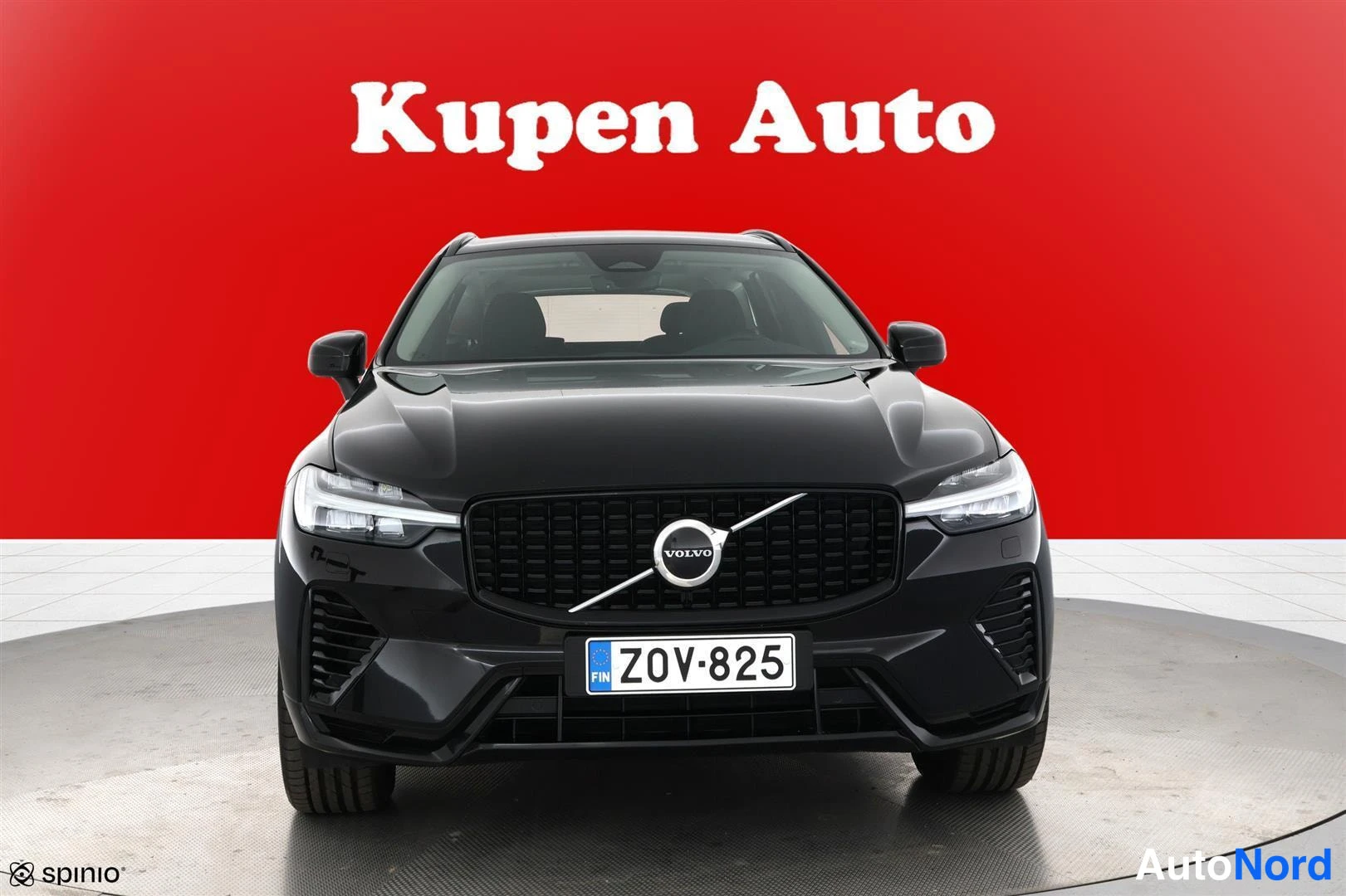 Edestä: Mustan Volvo XC60:n etunäkyvyys suoraan edestä punaisella taustalla, rekisterikilpi.