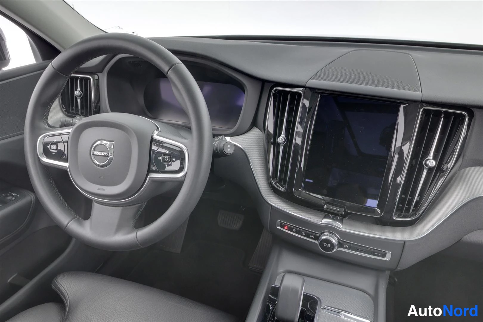 Muu: Lähikuva ohjaamosta: Volvo-merkillinen ohjauspyörä ja monitoiminapit, hallintalaitteet, keskellä pystysuora kosketusnäyttö ja ilmastointisuuttimet.