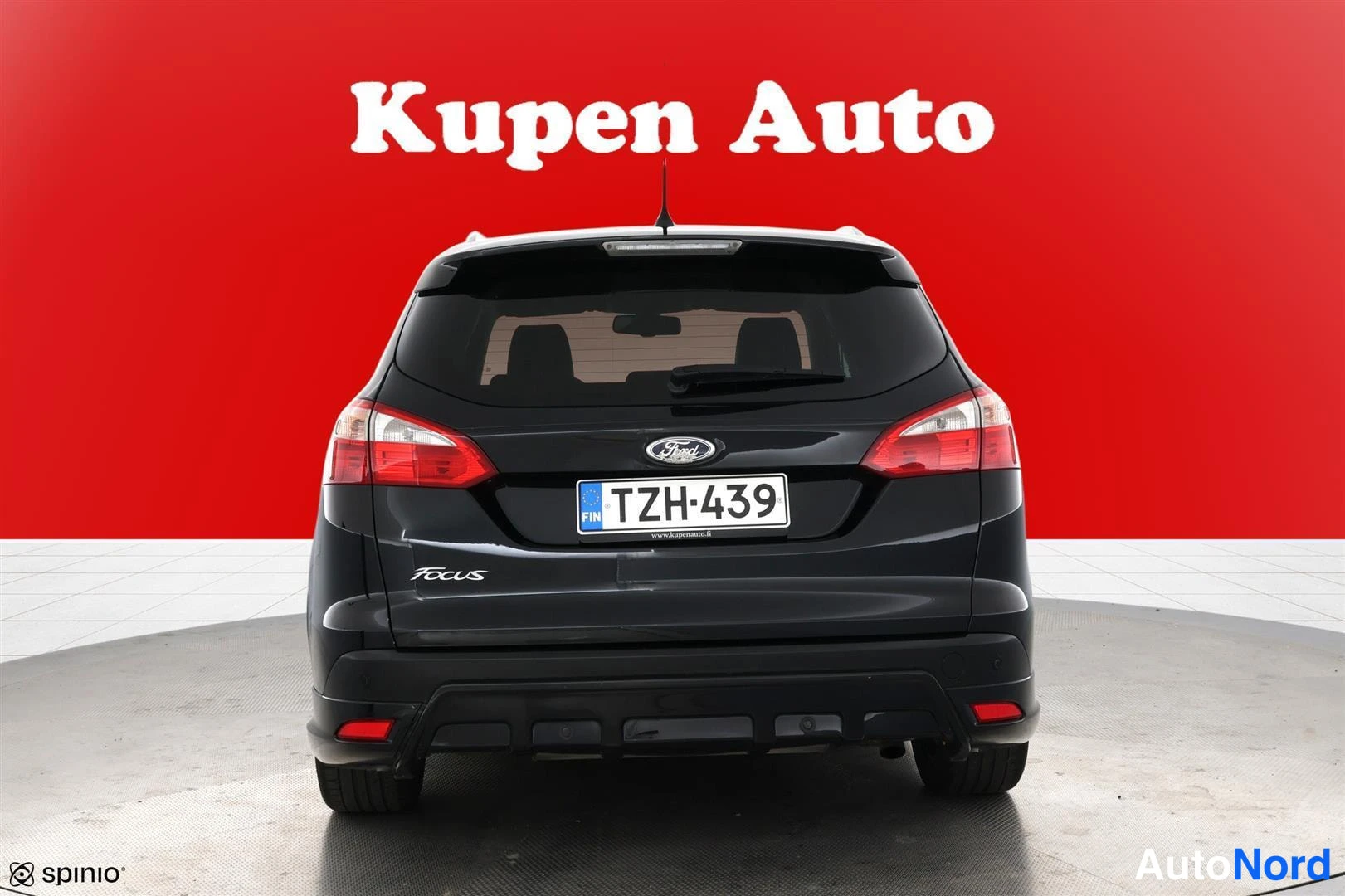 Takaa: Ford Focus -farmarin takaosa suoraan takaa, tumma koriväri, rekisteritunnus, punaisella taustalla.