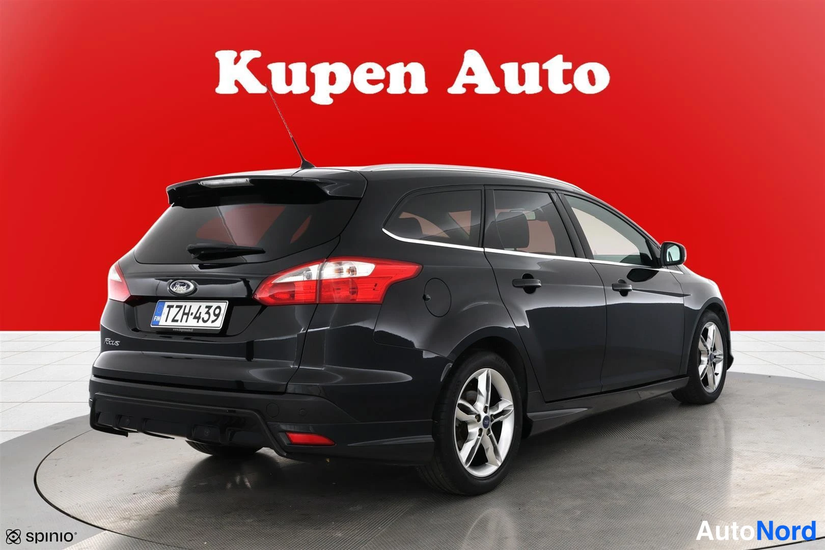 Takaviisto: Ford Focus -farmari kolmivartalokuva takaa vasemmalta, musta koriväri, hopeat vanteet, punainen tausta.