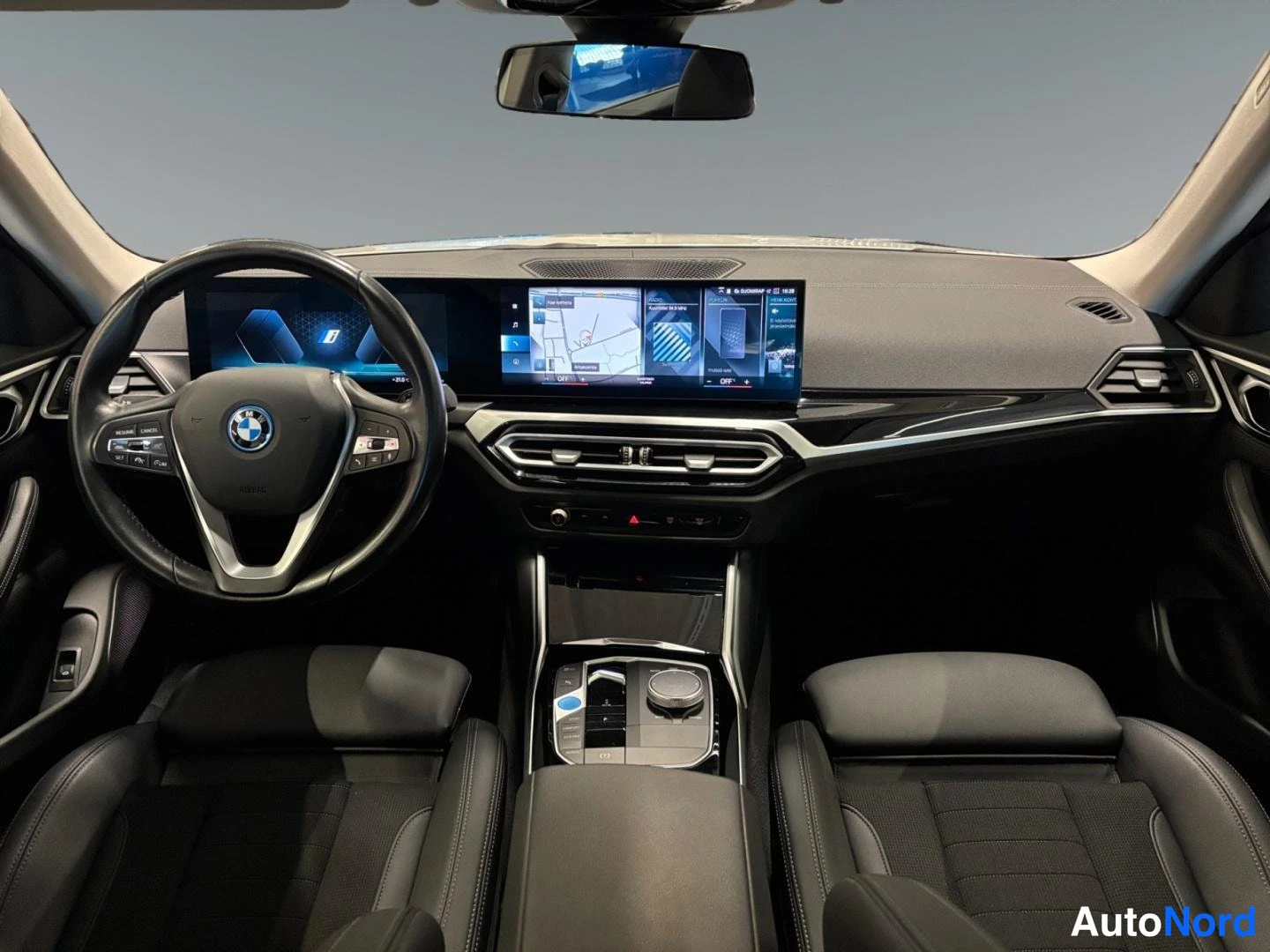 Muu: Ohjaamosta suoraan taakse: BMW-ohjauspyörä, laaja infotainment-näyttö ja keskikonsoli.