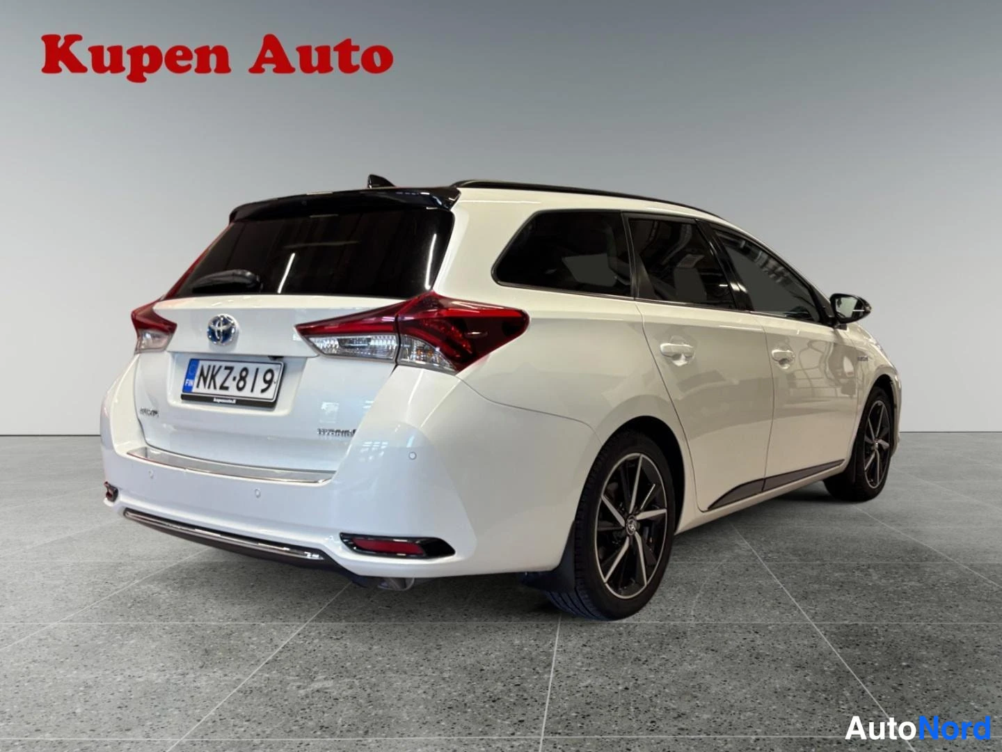 Takaviisto: Toyota Auris Touring Sports -farmari takaa vasemmalta kuvattuna,vaalea kermanvalkoinen koriväri,tummat vanteet ja -rekisterikilpi.