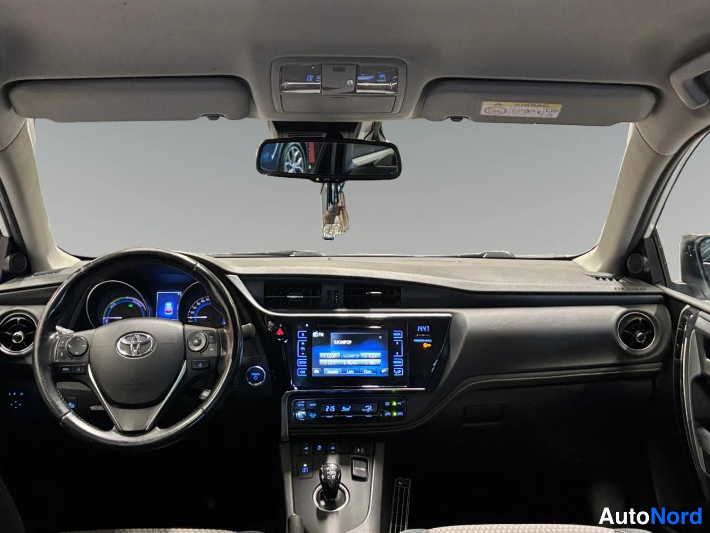 Yksityiskohta: Ohjaamo Toyota Auriksesta: ohjauspyörä, hybridimittaristo, kosketusnäyttöradio ja automaattivaihteisto.