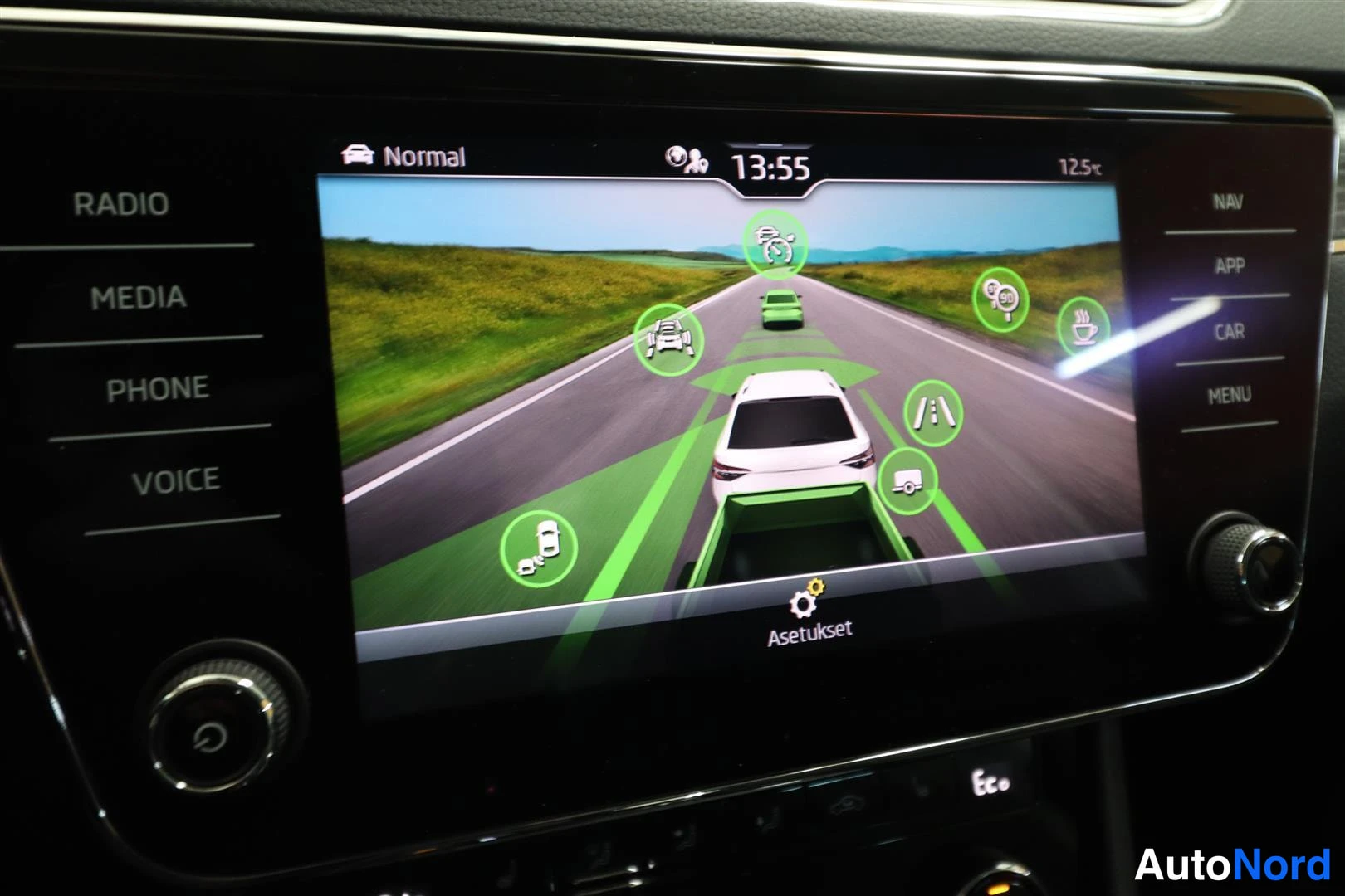Yksityiskohta: Auton infotainment-näyttö, jossa on kuvituskuva autosta moottoritiellä ja vihreitä turva-avustajien kuvakkeita ympärillä.
