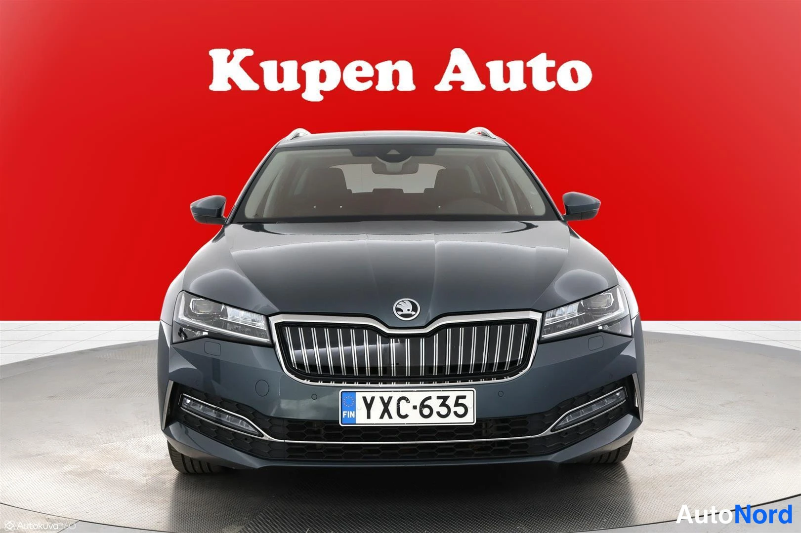 Edestä: Skoda Superb farmarin edessä kohti kameraa valokuvassa, punainen tausta ja Kupen Auto -teksti yllä.
