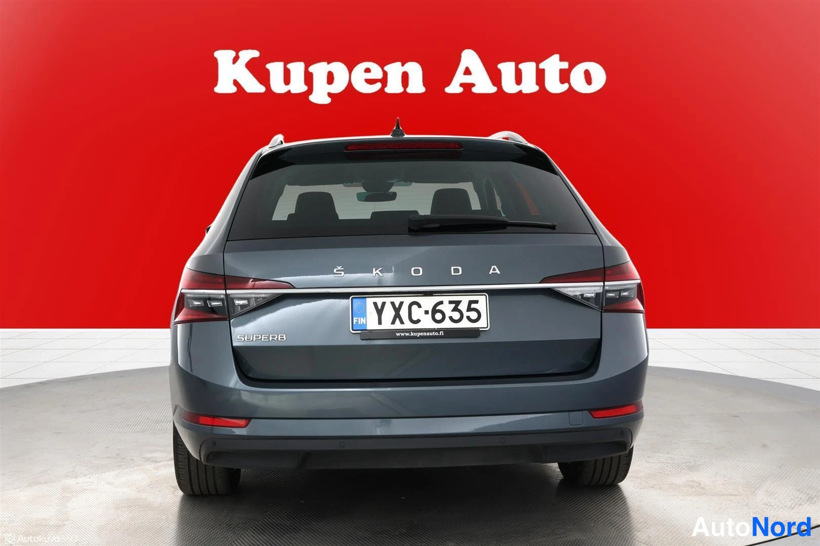 Takaa: Skoda Superb -farmari suoraan takaa, rekisterikilpi ja Škoda-teksti kannen reunassa.