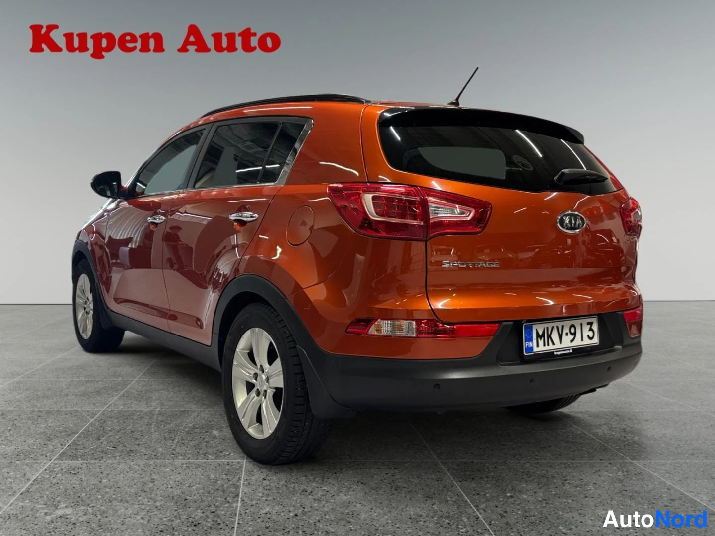 Takaviisto: Kia Sportage takaa oikealta kolmiväripisteenä; SPORTAGE-teksti ja rekisterikilpi näkyvissä.