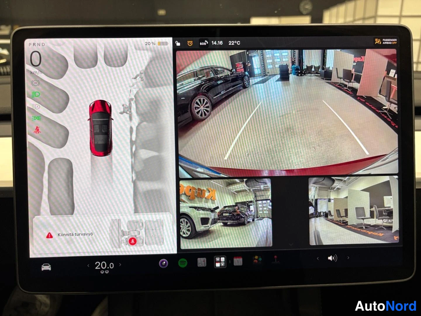 Muu: Tesla Model 3:n keskiconsoolin suuri kosketusnäyttö, jossa näkyy peruutuskamera ja ympärivuo­raisten kameroiden kuvat pysäköintitilanteessa sekä varoitus 'Kiinn