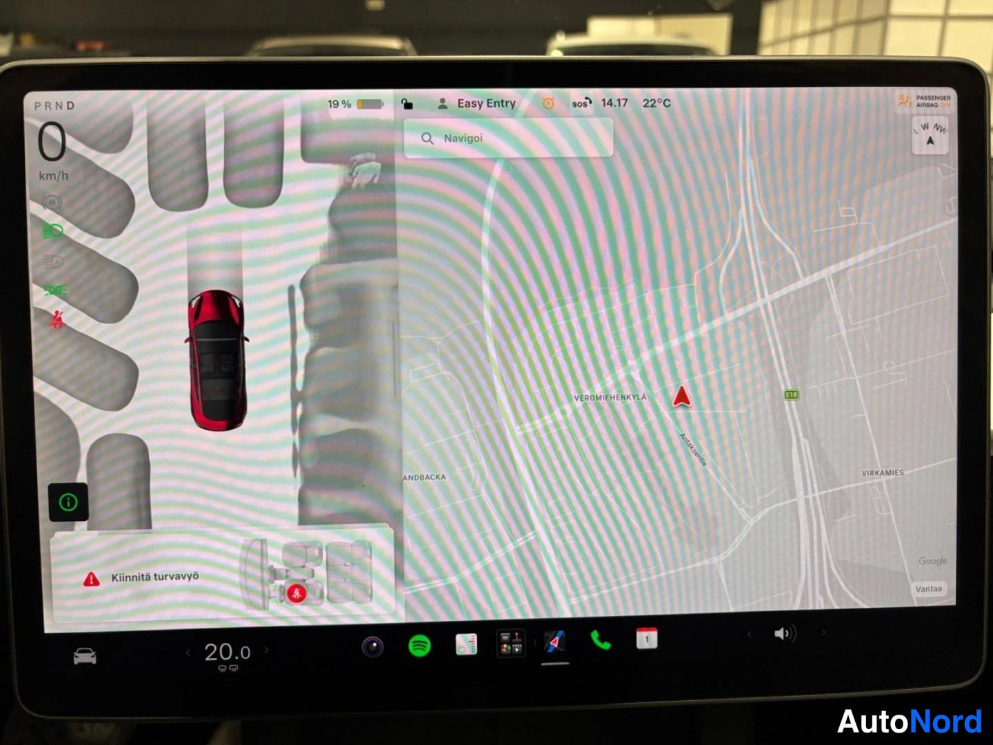 Muu: Tesla Model 3:n kosketusnäyttö, vasemmalla pysäköintigrafiikka, oikealla navigointikartta; varoitus 'Kiinnitä turvavyö' ja akun varaus 19 %.