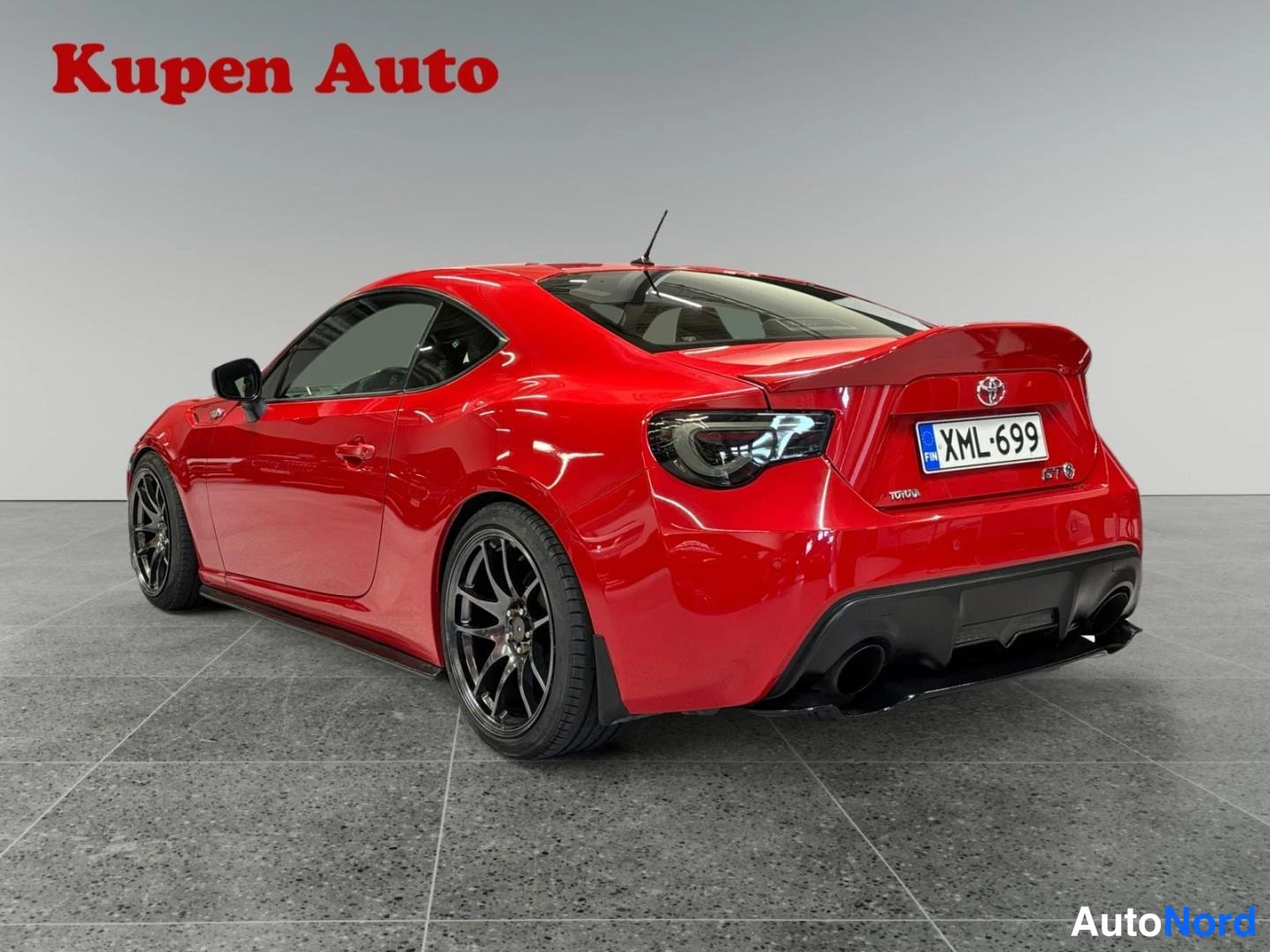 Takaviisto: Punaisen Toyota GT86:n taka-kolmasonäkö vasemmalta, tummat vanteet, kaksoispakoputket ja rekisteri.