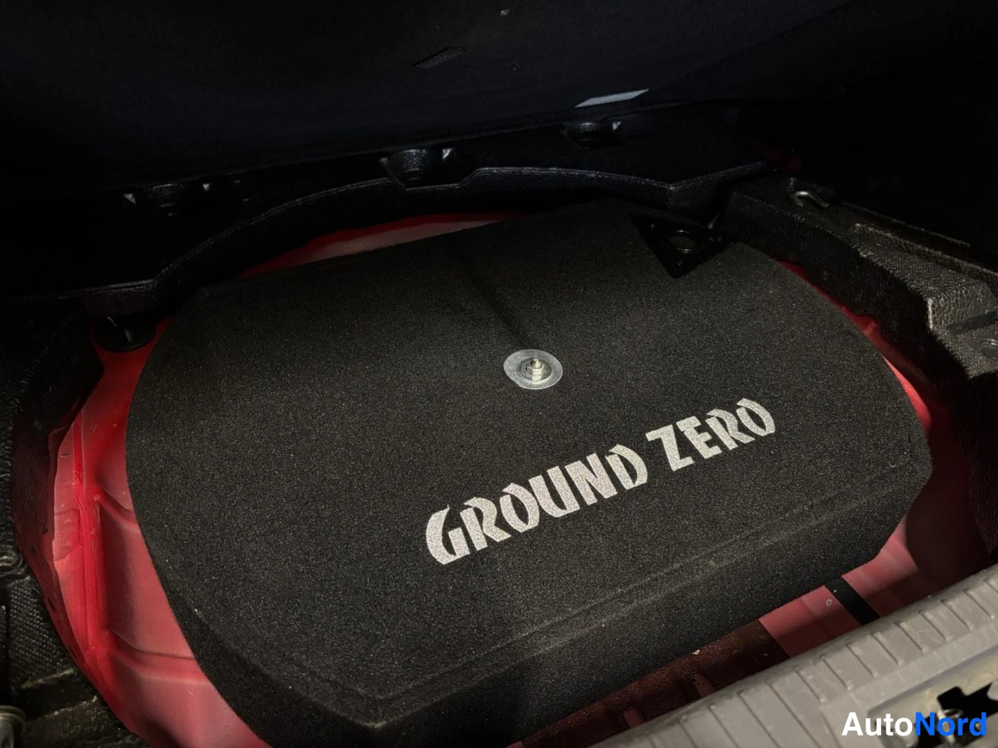 Muu: Musta GROUND ZERO -tekstillä varustettu subwoofer-kaiutin tavaratilan sivutilassa.