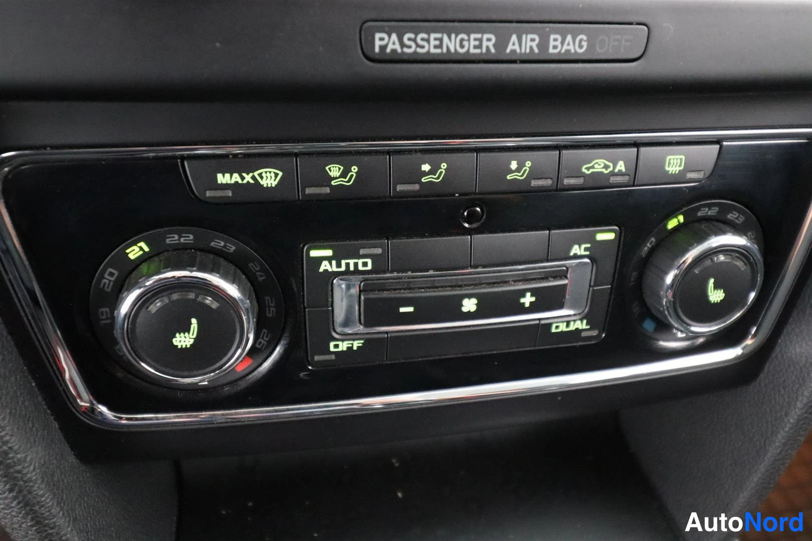 Yksityiskohta: Auton ilmastointipaneeli, jossa kirjoitus PASSENGER AIR BAG OFF, kaksi säätönuppia ja painikkeet Auto, AC, Dual ja Off.