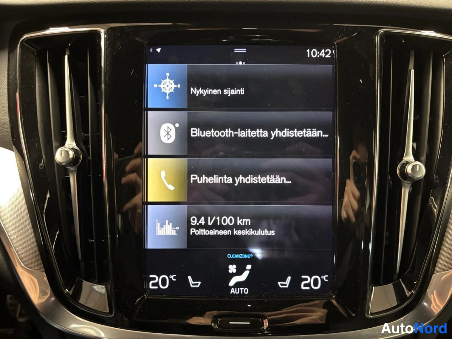 Muu: Pystysuoran keskinäytön tarkka lähikuva: valikossa rivit 'Nykyinen sijainti', 'Bluetooth-laitetta yhdistetään…', 'Puhelinta yhdistetään…' ja '9.4 l/100 km Poltt