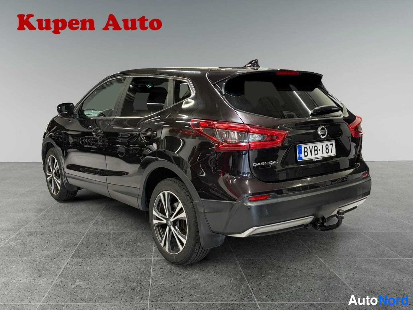 Takaviisto: Nissan Qashqai -käyttöauton takakulmanäkymä vasemmalta: tummanruskeaa metalliväriä, rekisterikilpi, luukulla Qashqai-teksti ja Nissan-merkki, takana vetokoukku.