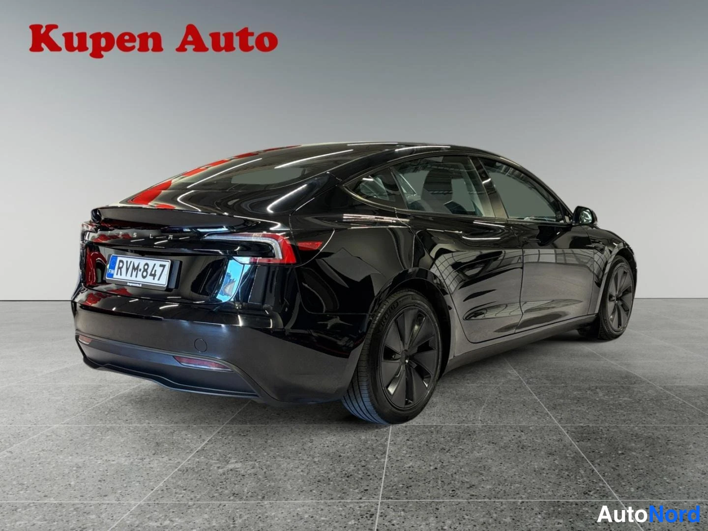 Takaviisto: Musta Tesla Model 3 -henkilöauto takaviistosta sisätiloissa, rekisteritunnus.
