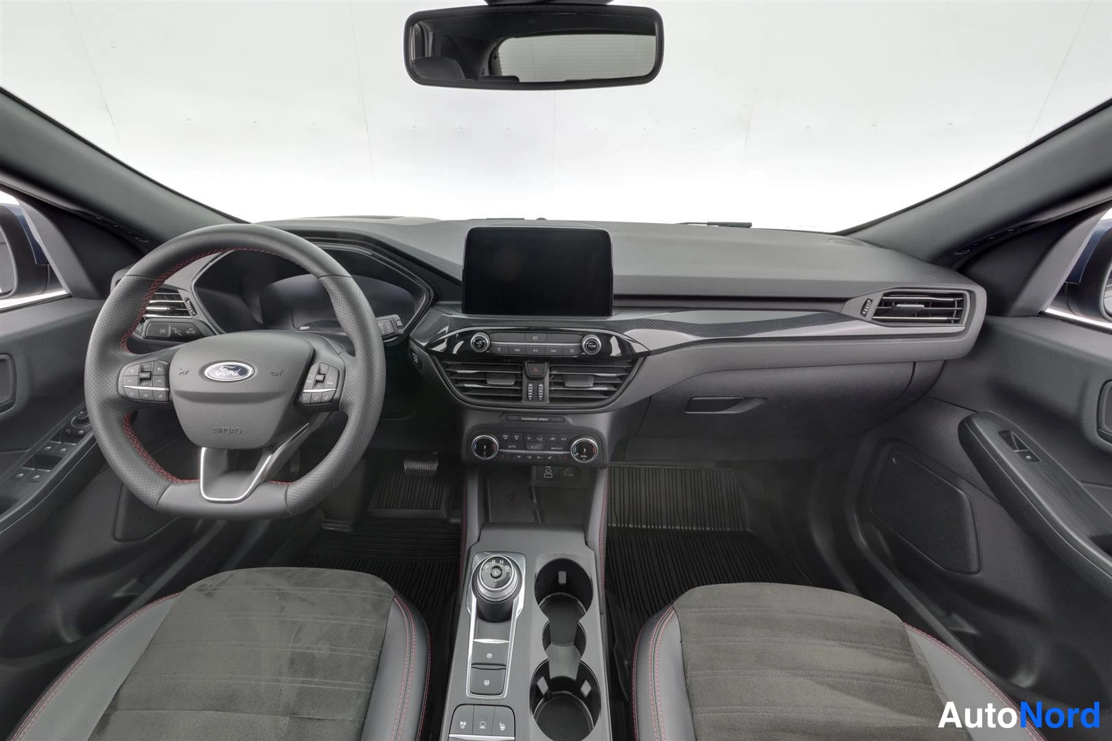Muu: Musta auton ohjaamo edestä: kuljettajan ratin Ford-logo, keskikonsolissa kosketusnäyttö, vaihteenvalitsin ja kaksi kuppikestoa, etupenkit alareunassa.