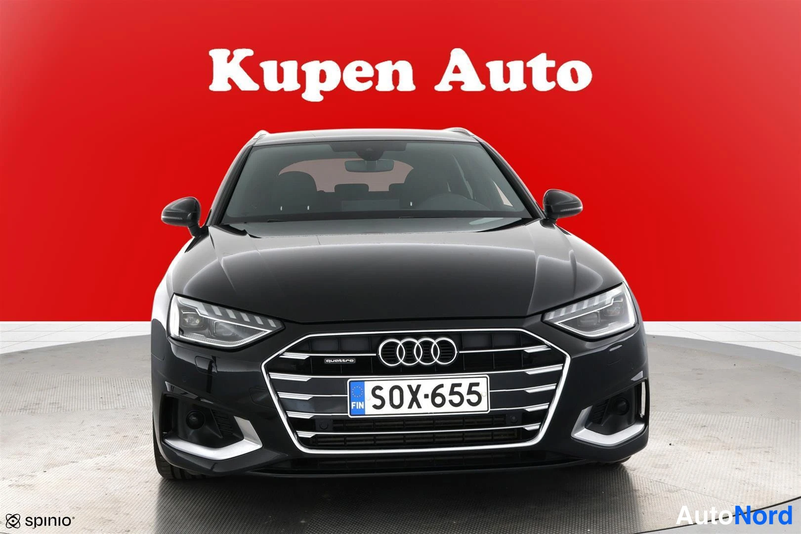 Edestä: Mustan auton etunäkymä, grille ja rekisterikilpi punaisella taustalla.