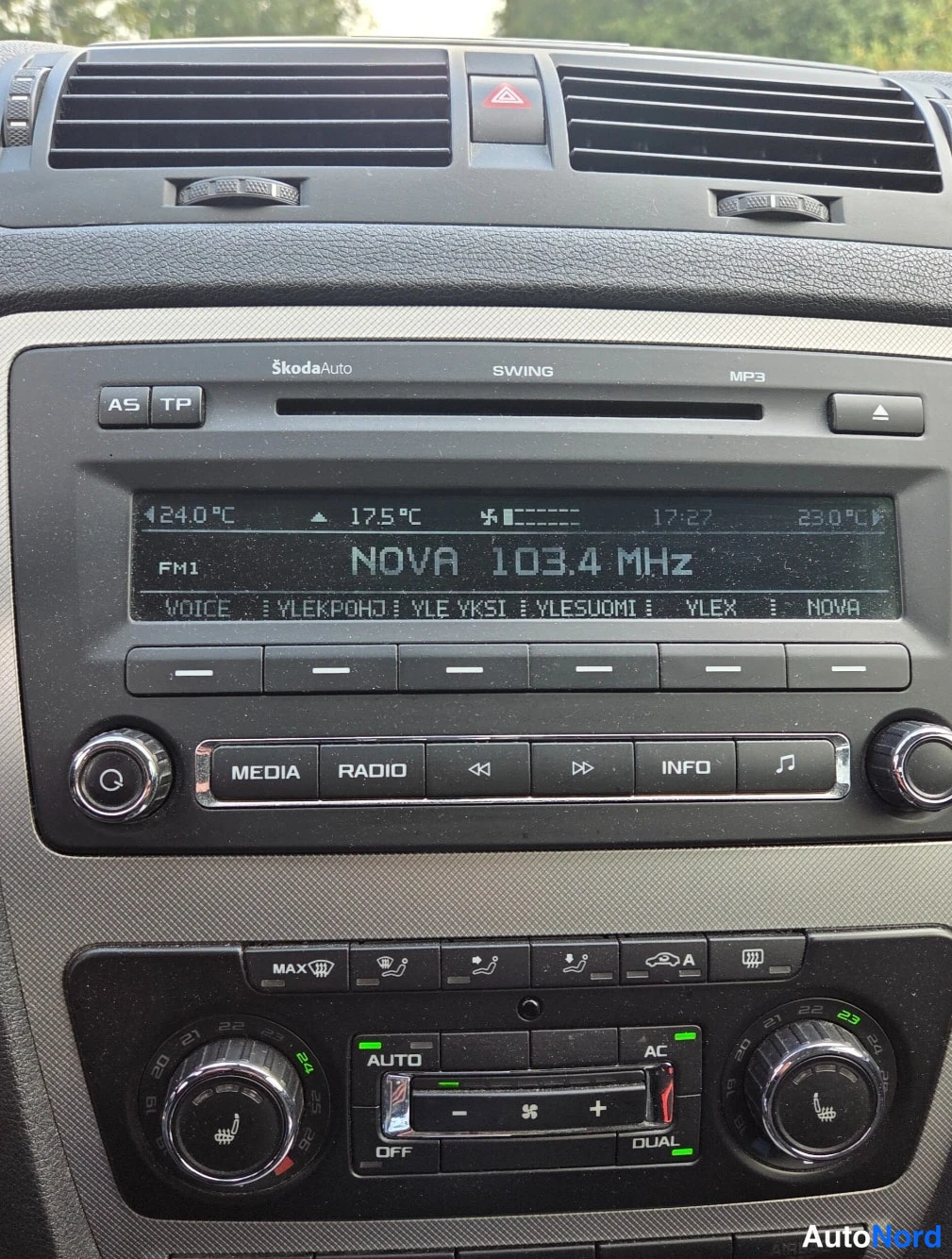 Yksityiskohta: Kojetaulun keskikonsoli lähikuvassa: Škoda Swing -radio, kaksipiirinen ilmastointi (AUTO/AC/DUAL) ja lämmitettävien istuimien merkkivalot.