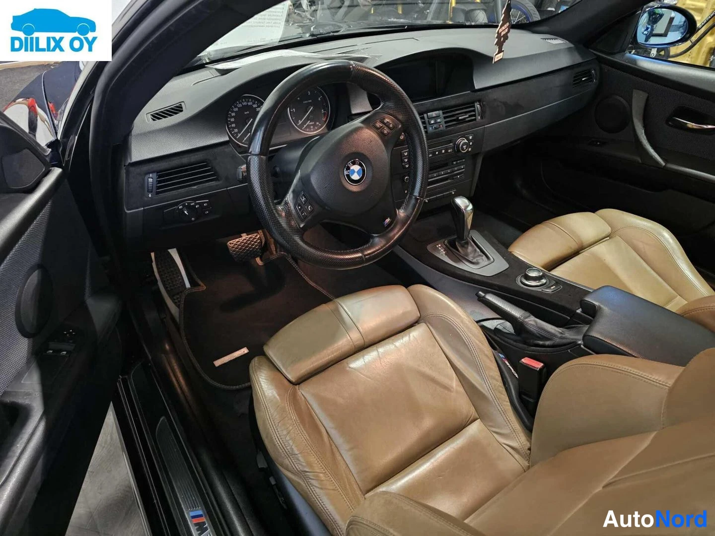 Muu: Ohjaamo yläviistosta: BMW-ohjauspyörä, kojelauta ja mittaristo, automaattivaihteiston valitsin sekä beigen väriset nahkaiset istuimet.