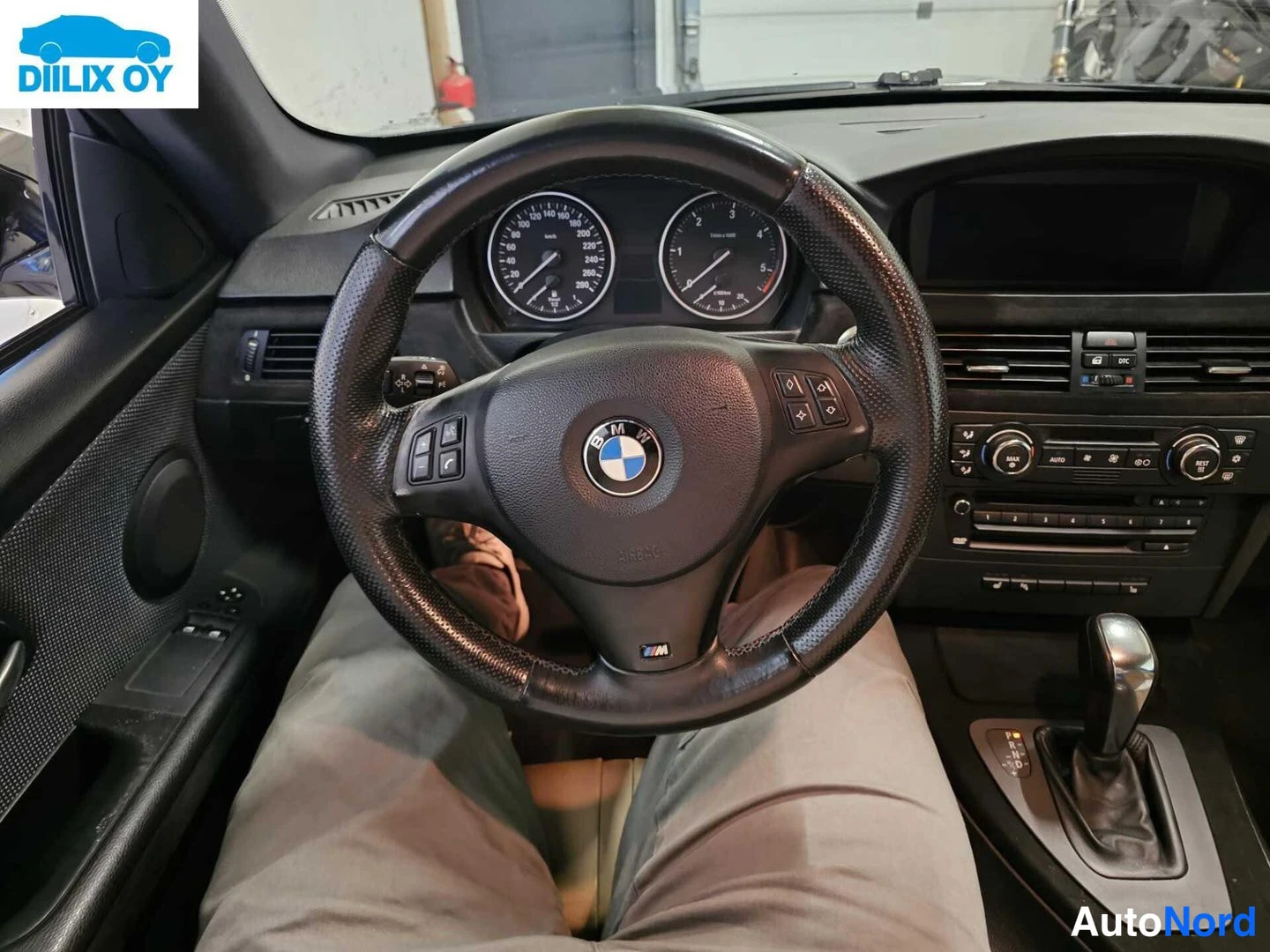 Sivulta: Sisäkuva kuljettajan paikalta: BMW-ohjauspyörä M-merkillä ja monitoimipainikkeilla, analogiset mittarit sekä automaattivaihteen valitsin keskikonsolissa.