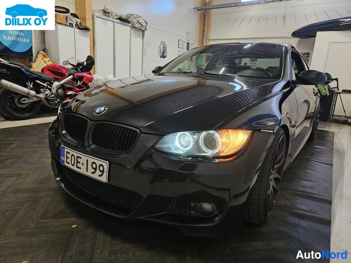 Etuviisto, nokka vasemmalle: Etuna näkyvä musta BMW-kupé sisätiloissa, jossa auto kääntyy oikealle päin eteenpäin. Valojen renkaat (halogeni) palavat, jalkineet ja edessä oleva val