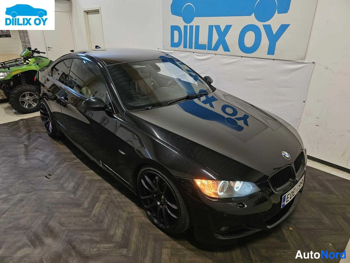 Etuviisto, nokka oikealle: Musta BMW-kupé nähtynä etuvasemmassa kolmasosakulmassa. Autossa on lasikatosta, joissa on sininen logo sekä mustat pyörät. Taustalla on vihreä nelipyörä.