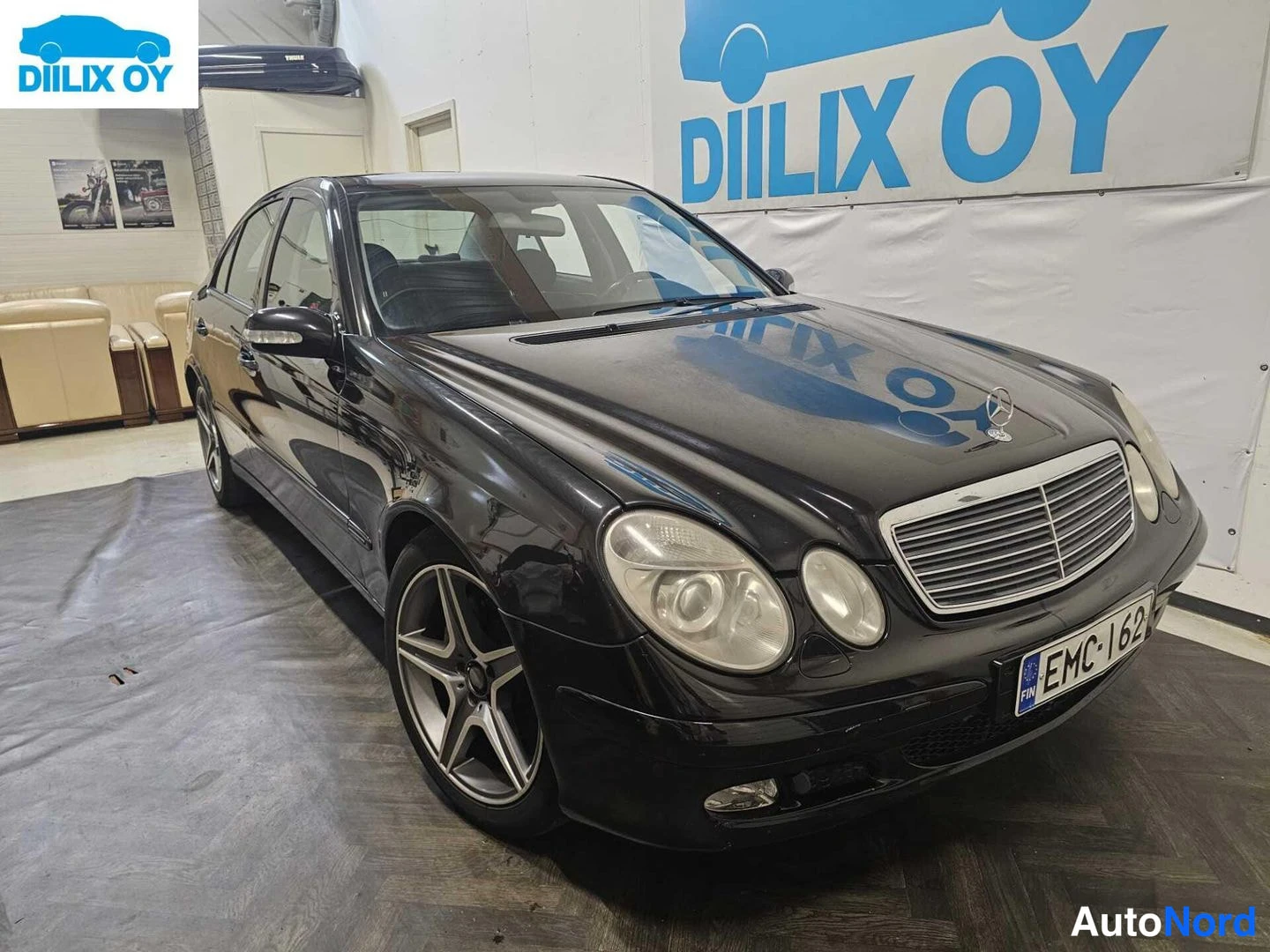 Etuviisto, nokka oikealle: Musta Mercedes-Benz E-sarjan sedan esittelytilassa. Etuvalot ja grilli näkyvät.