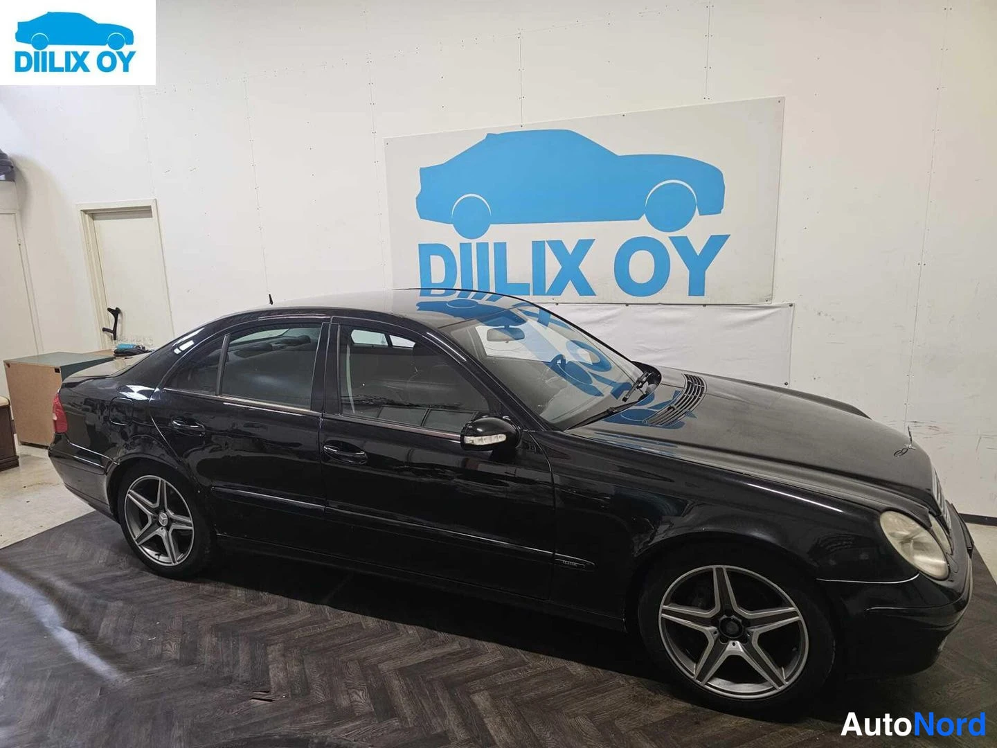 Sivulta: Musta Mercedes-Benz E-sarjan sedan esittelytilassa. Autosta näkyy vain sivu.