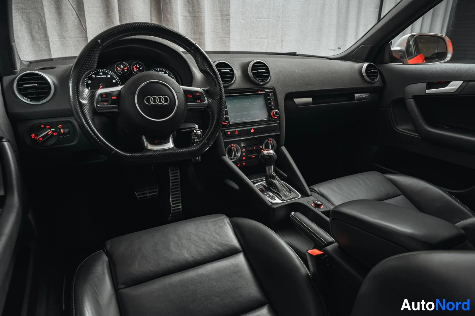 Ohjaamo: Audi-merkillä varustettu ohjaamo: monitoimiohjaus, näyttö keskikonsolissa, mustat istuimet ja automaattivaihteen valitsin.