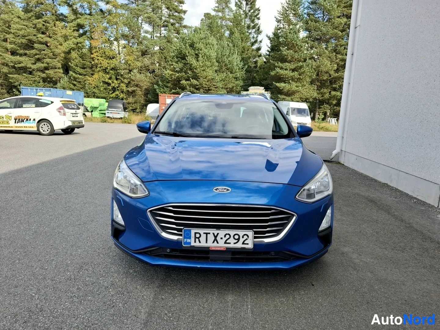Edestä: Sinisen Ford Focus -farmariauton etänä suoraan edestä otettu kuva, rekisterikilpi.