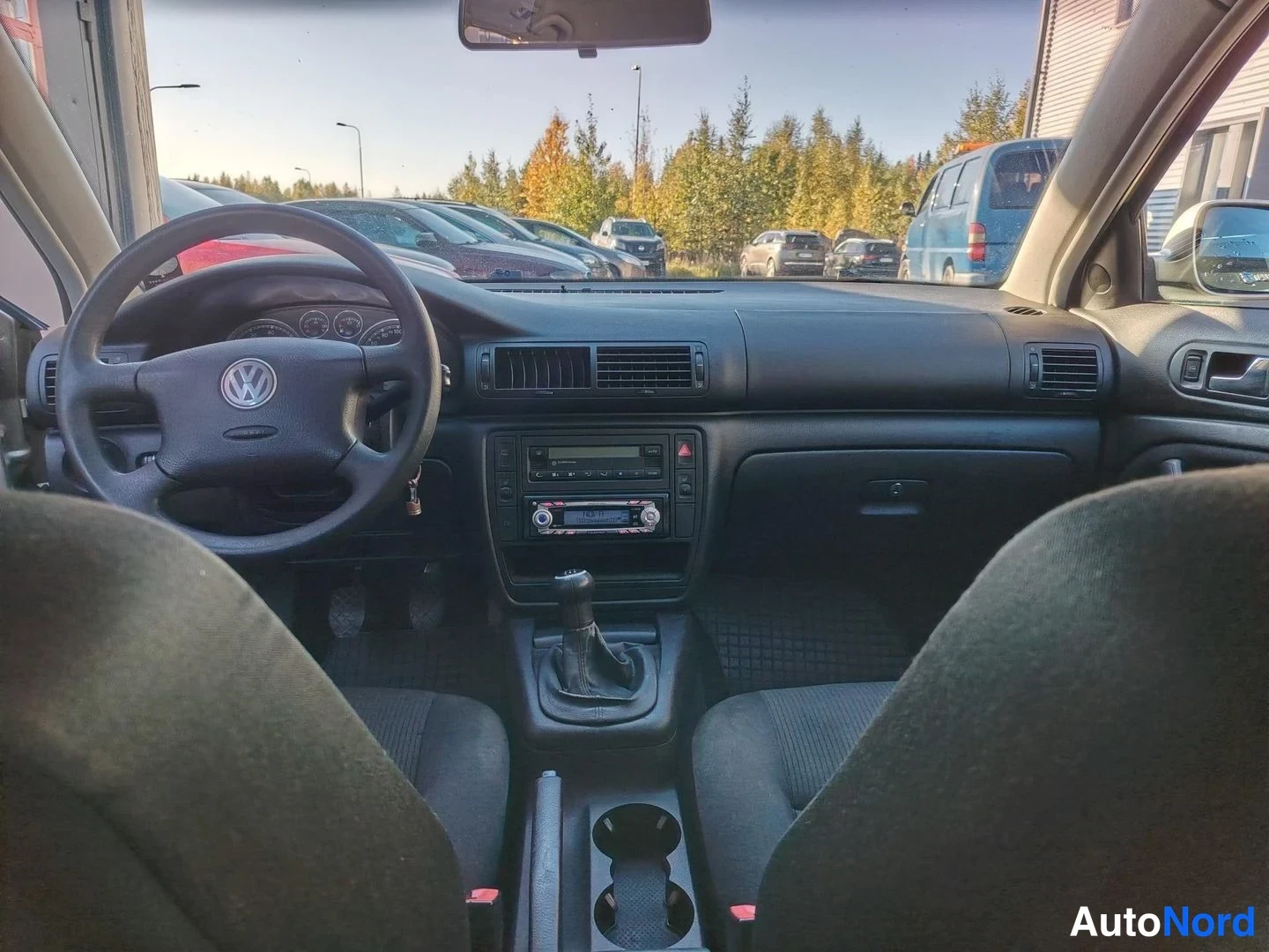 Muu: Sisätila-kuva Volkswagenin ohjaamosta: kuljettajan sivulla VW-merkillä varustettu ohjauspyörä, keskikonsolissa radio ja käsivaihteaja, näkyvissä myös etumatkust