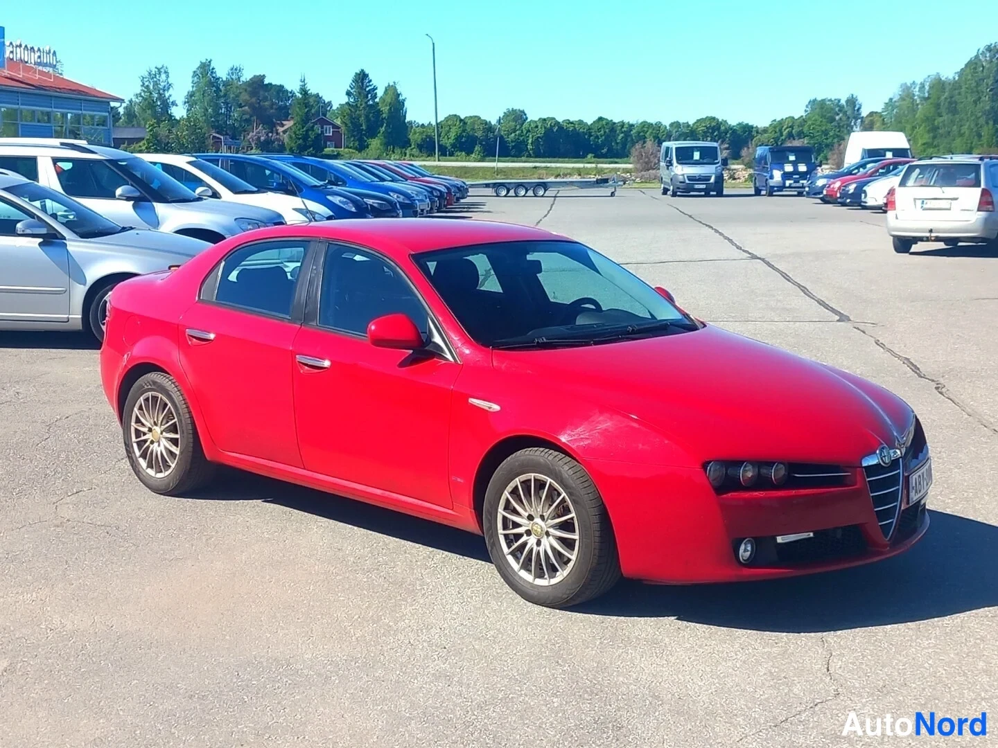 Etuviisto, nokka oikealle: Punainen Alfa Romeo 159 -sedan etuokoliskuva autopaikalta, keula oikealla puolella.