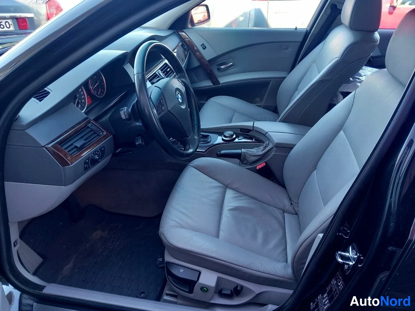 Edestä: Kuljettajan näkökulma auton sisätiloihin: BMW-ohjauspyörä, mittaristo ja harmaat istuimet.