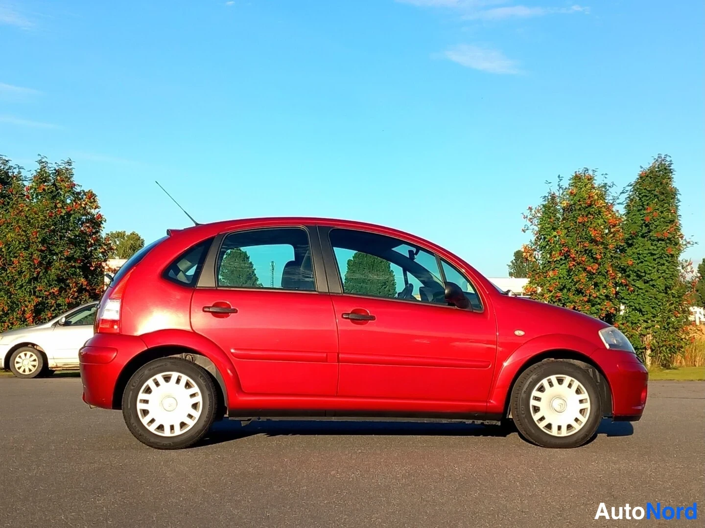 Sivulta: Punainen viisiovinen hatchback sivulta kuvattuna aurinkoisella parkkipaikalla.