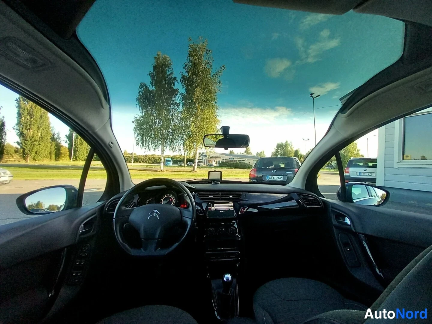 Yksityiskohta: Matkustamon näkymä Citroënin ohjaamosta: panoramic-tuulilasi, ohjauspyörä, keskikonsolin näyttö ja vaihtajanuppisesta päätellään manuaalivaihteisto.