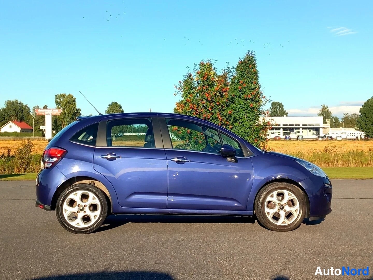 Etuviisto, nokka oikealle: Sininen Citroën C3 -henkilöauto sivulta oikeasta etukulmasta, kylki ja etuosa avoimella parkkialueella.