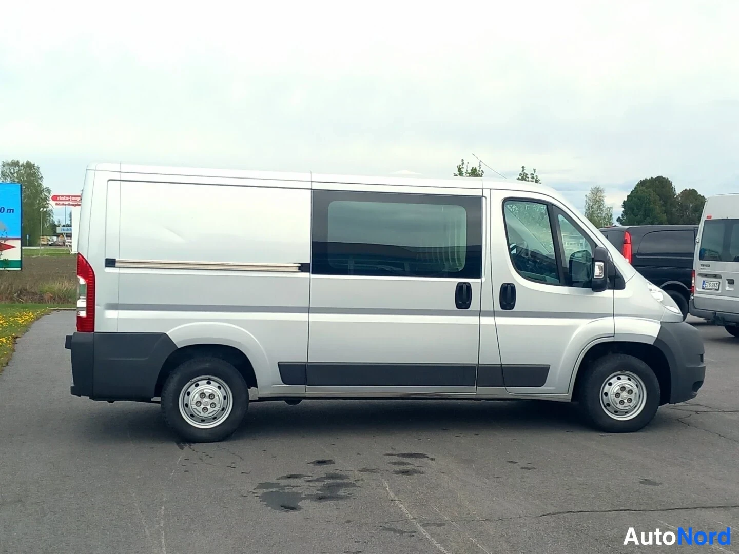 Sivulta: Hopeanharmaa pakettiauto sivulta, liukuovi ja takaovet näkyvät.