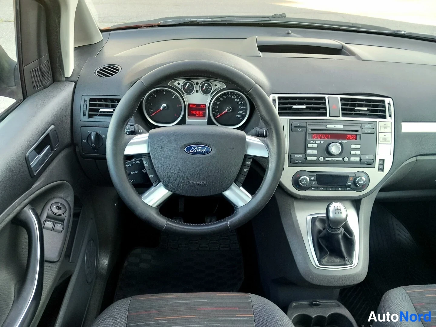 Yksityiskohta: Ford-merkkisen auton ohjaamo: kuljettajan ohjauspyörä, mittaristo ja keskikonsolin radio sekä manuaalivaihteiston vaihdekeppi.