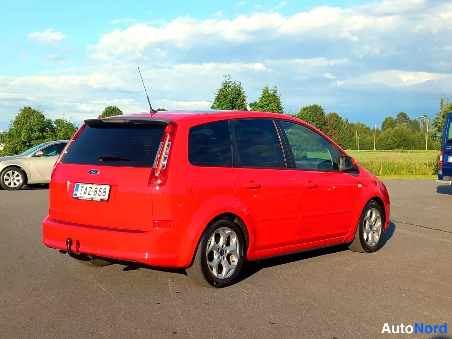 Takaviisto: Punainen tilavautomobiili takaviistosta, korotettu takaosa ja rekisteritunnus näkyvissä.